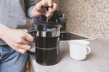 Woman prepares coffee in a French press in her kitchen. Preparing ground coffee in a press. Refreshing drink for breakfast.
