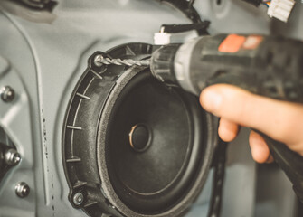 A car repairman repairs a car door. The car mechanic drills the car speaker out of the door. Work with a drill.	