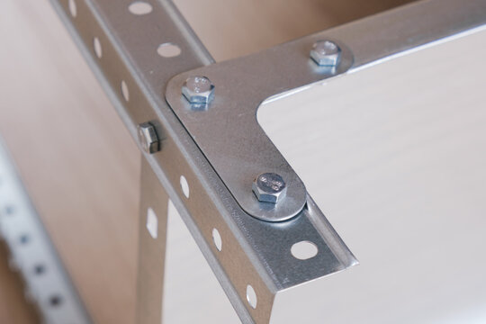 Metal L-shaped corner bracket for fixing parts of a prefabricated structure. Fixing part of a metal rack, fixed with bolts. Close-up, selective focus - Powered by Adobe