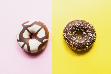 Two doughnuts with chocolate glaze on a pink and yellow background. Top view.
