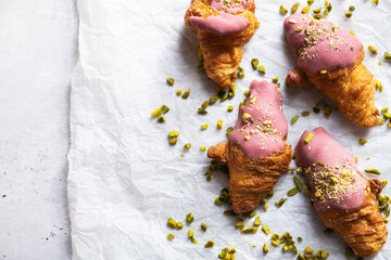 Mini-croissants with ruby chocolate and pistachios on a baking paper, gray background. Top view and copy space. - 495528505
