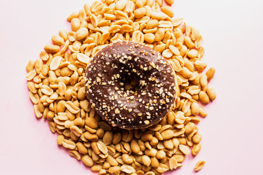 Doughnut with chocolate glaze and peanuts on a pink background. Top view.