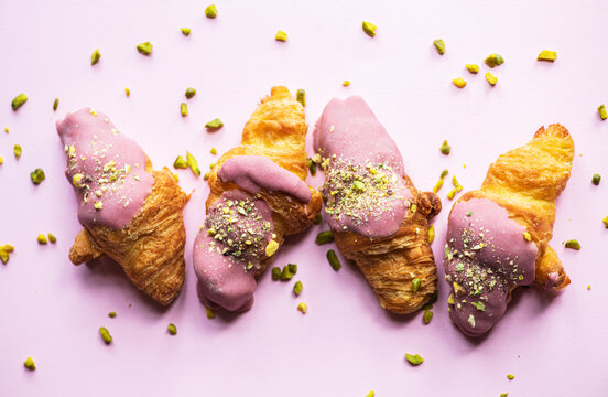 Mini-croissants with ruby chocolate and pistachios on a pink background. Top view.
