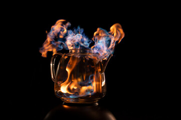 Fire within a see through glass tea pot showing beautiful orange and blue flames inferno giving the idea of substance or alcohol abuse.