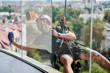 Industrial mountaineering cleaning service worker hanging on rope and wiping window. View from...