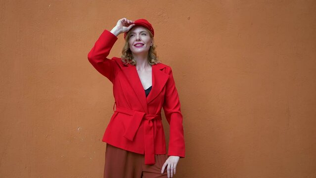 Stylish blonde girl in red jacket posing against the background of terracotta wall.