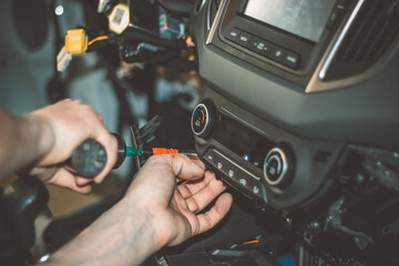 An auto electrician, mechanic or technician repairing the internal wiring system of a car. The concept of a car service. Selective focus a man working during the repair of a car in the workshop. 