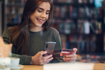 Woman using smartphone and a credit card for online shopping in a cafe