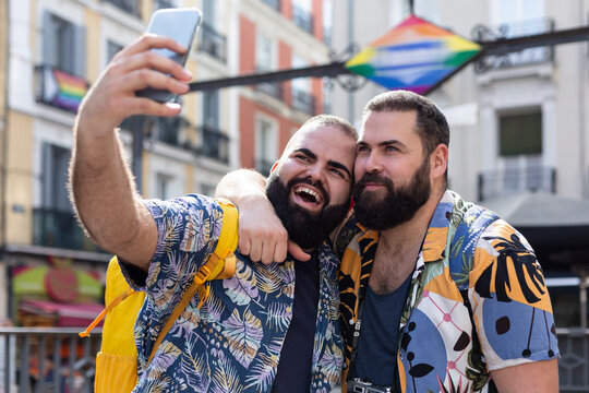 Two gay men on vacation taking a photo together with mobile phone during a sightseeing tour in a city. Lgbt couple traveling.
