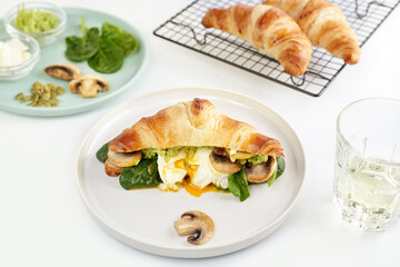 Breakfast or lunch concept photography. Croissant with ingredients egg, mushrooms, avocado sauce, spinach on plate and glass of vine