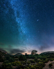 Panoramic view of the Milky Way and the Andromeda galaxy over a rock arch shaped like a turtle. Night landscape