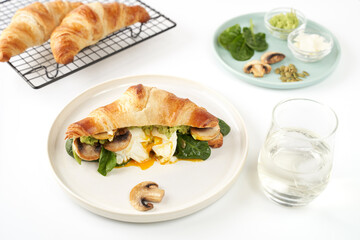 Breakfast or lunch concept photography. Croissant with ingredients egg, mushrooms, avocado sauce, spinach on plate and glass of vine