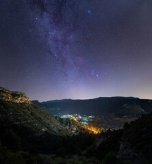 The milky way over an illuminated town. Night landscape with the milky way, orion and the pleiades