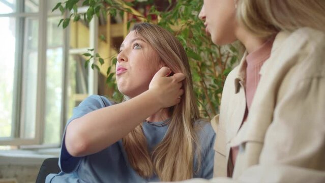 LGBT women sit together in the living room, talk to each other, smiling, and one of them touches her girlfriend's hair