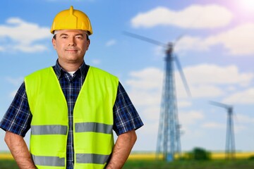 Beautiful man in white helmet working with digital tablet at energy farm. Male inspector controlling functioning of wind turbines outdoors.