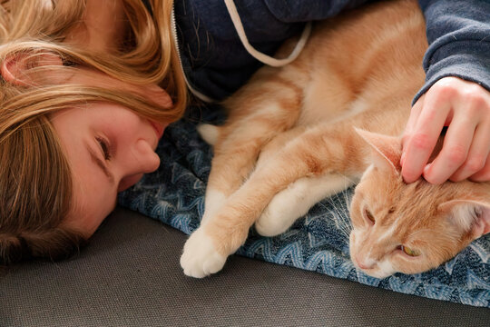 An Young Adolescent girl lying on a couch finds comfort by snuggling close to and petting her cat