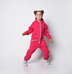 girl in a pink jumpsuit with a hood and reflective safety stripes stands facing the camera and...