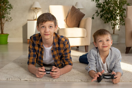 Portrait of two boys lie on the floor in a room playing video games with joysticks
