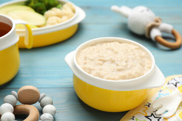 Toys and plastic dishware with healthy baby food on light blue wooden table, closeup
