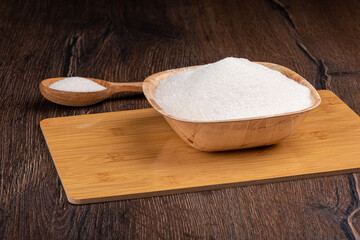 White sugar in wooden bowl and spoon over wooden background.