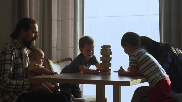Small Kids Children playing tiny jenga with her parents at table, jenga tower falls apart, Family have great time together play game at home in sunny room Day, happy childhood, Friendship concept