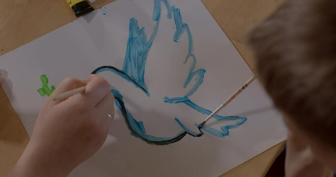 Hands paint the poster with dove and olive branch as a symbol of peace and innocence. Creative realisation of a person. Paint with a brush.