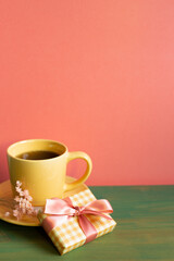 Yellow gift box and cup of coffee on green wooden table. pink wall background. copy space
