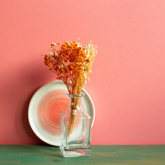 Vase of orange gypsophila dry flower on green wooden table. pink wall background. home interior