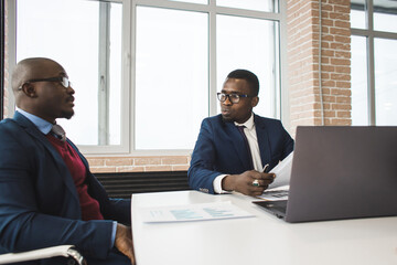 Two dark-skinned partners of an African American businessman in a meeting work on a laptop in the office. Affordable private courses and distance learning. New opportunities online