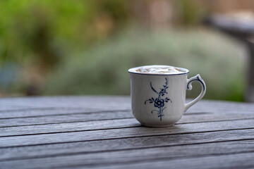 cup of coffee on wooden table in the garden, whipping cream on top, copy space