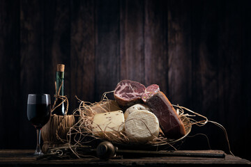 Assorted homemade cheese, salumi on wooden table with a wooden background
