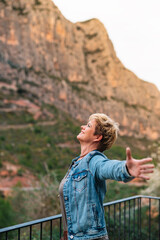 portrait of adult blonde short haired woman on holiday enjoying the scenery with her arms outstretched in freedom.