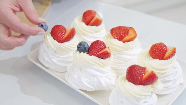 close up. cook decorates cakes anna pavlova with strawberries and blueberries 