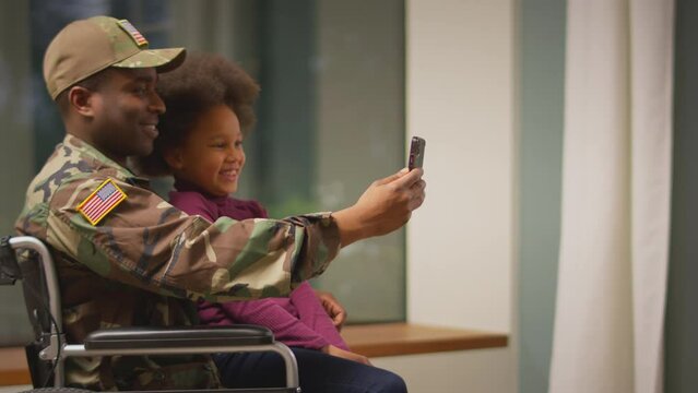 Injured American soldier wearing uniform in wheelchair posing for selfie and pulling faces on phone with daughter - shot in slow motion