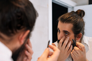 Young man applying eye make-up in the bathroom. Using eyeliner pencil
