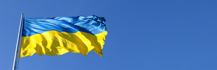 Large banner with the national flag of Ukraine flutters in the wind against the blue sky. Sunny day. Freedom and patriotism. Copy space