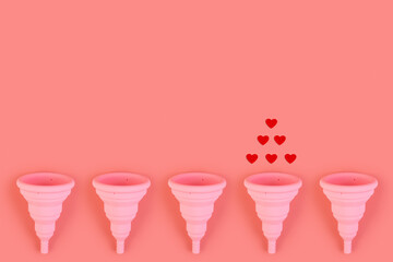 Silicone pink menstrual cup flat lay. Women's health and alternative hygiene. Cups with drop of blood or red hearts on a pink background. eco-friendly, Alternative reusable product for female hygiene.