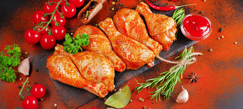 Marinated product, quick cooking.Barbecue marinated chicken dramstik on a black cooking board, with fresh rosemary leaves and fresh cherry tomatoes and various spices, close-up.Semi-finished product.