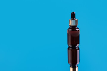 glass brown bottle with pipette with essential oil on isolated blue background. Aromatic cosmetic product for skin and hair care Moisturizing beauty product with organic natural oil.