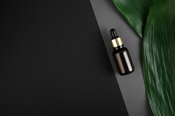 glass brown bottle with pipette with essential oil on a grey, black geometric background with green tropical leaves top view. Aromatic cosmetic product for skin and hair care Moisturizing beauty.