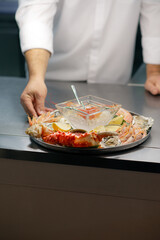 The chef serves a plate of cooked seafood on a bright table. Red salmon caviar, crab, shrimp, scallops, octopus
