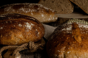 horizontal photo of artisan breads cut from wholemeal flour with jar of flour on rustic wooden table and black background