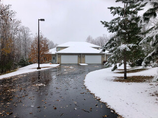 Asphalt driveway leading to a twin home or duplex has many wet leaves on it, following a recent snow fall, on an overcast autumn day in Minnesota.