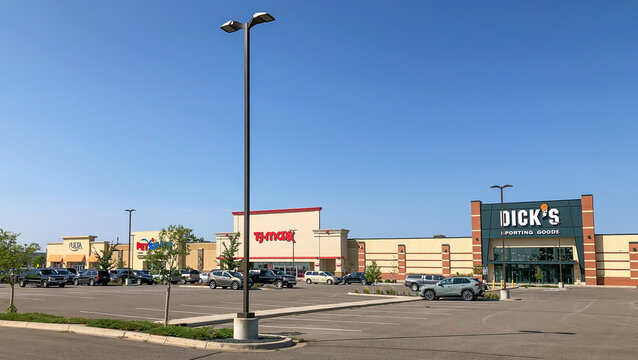 BAXTER, MN - 1 SEP 2021: Strip mall and parking lot with cars in front of the stores, and a light post extending toward the blue sky on a sunny day in Minnesota.