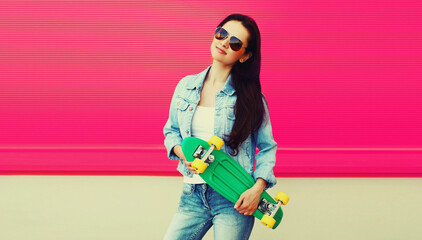 Portrait of brunette woman with green skateboard on colorful pink background