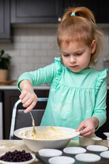Small kid cooking in kitchen. Little girl making dough for muffins with berries, helping mother
