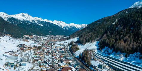 Ski resort town of St. Anton am Arlberg in Austria with amazing winter sunny sky and snowy mountains covered with pine trees in the background - obrazy, fototapety, plakaty