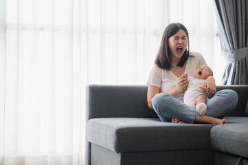 Obraz premium Tired Asian mother and her baby girl yawns together while sitting on sofa at home