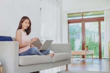 Beautiful Asian woman working with laptop notebook at home on sofa