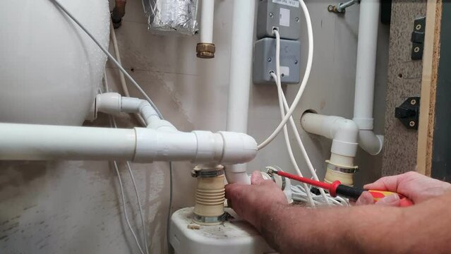 Plumber getting wet while fixing a leak on a macerator waste pipe with a screwdriver